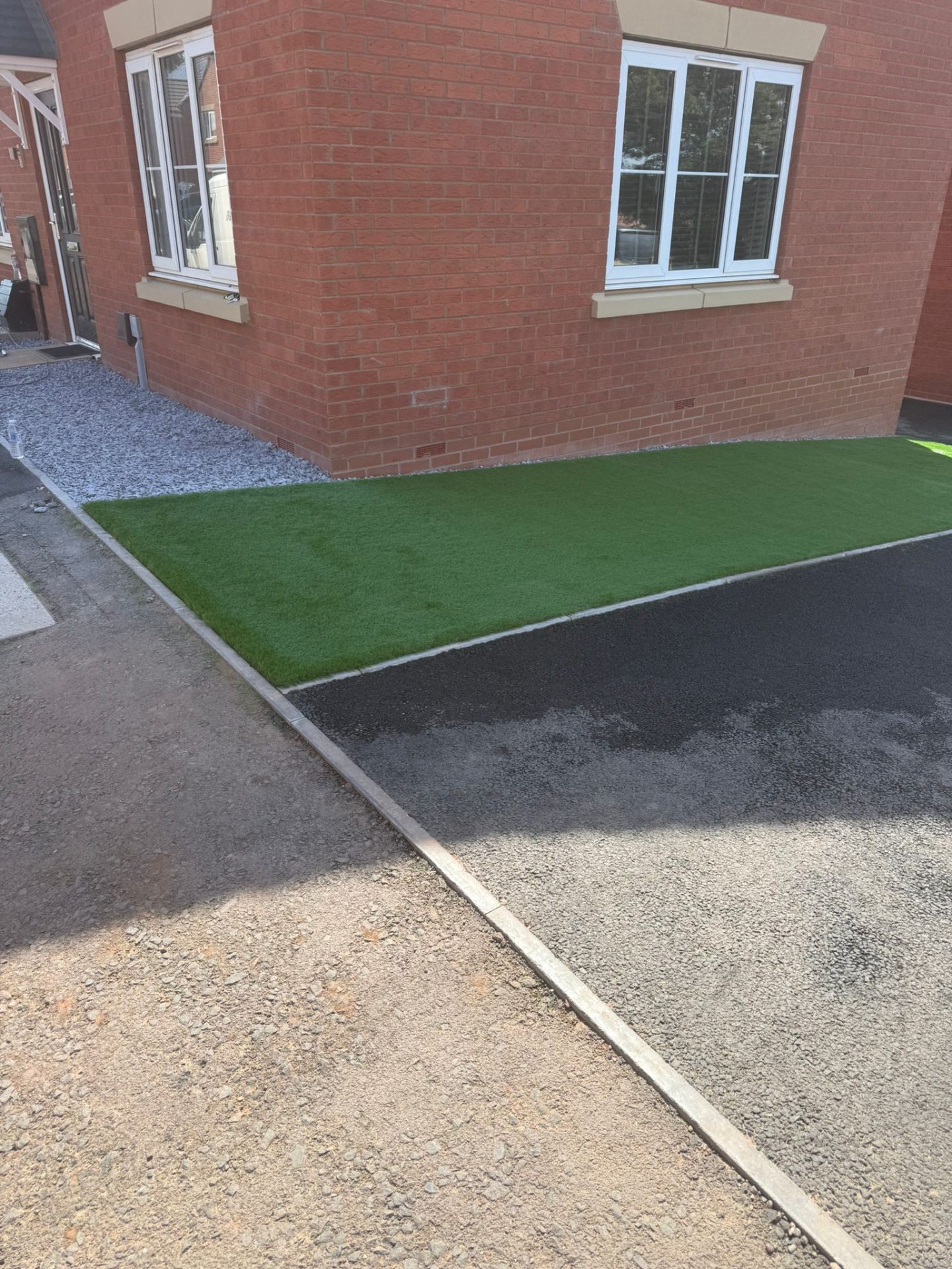 Freshly laid artificial grass lawn with kerb edging alongside new tarmac drive