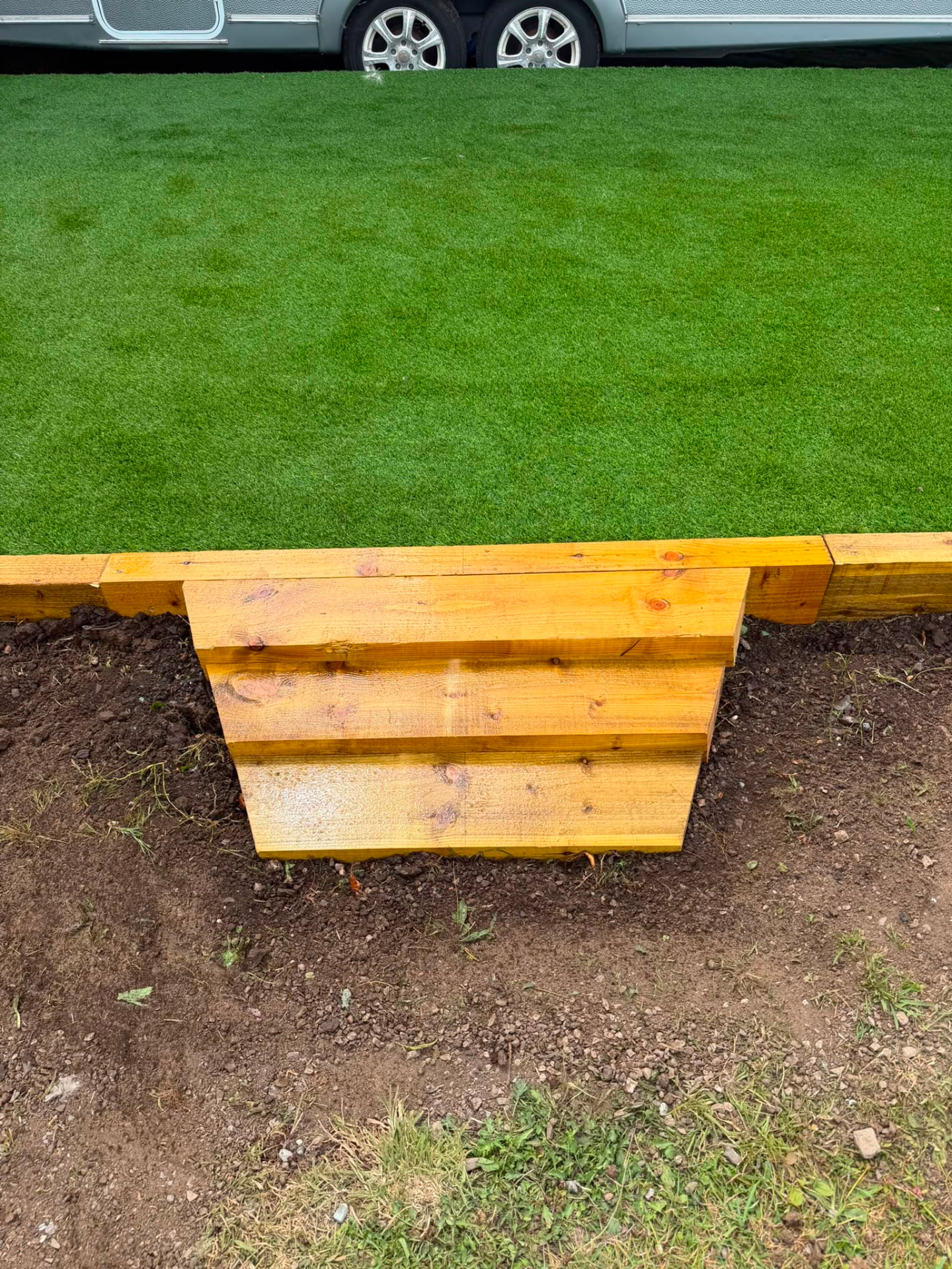 Close-up of artificial grass edge with timber sleeper retaining edging and step detail
