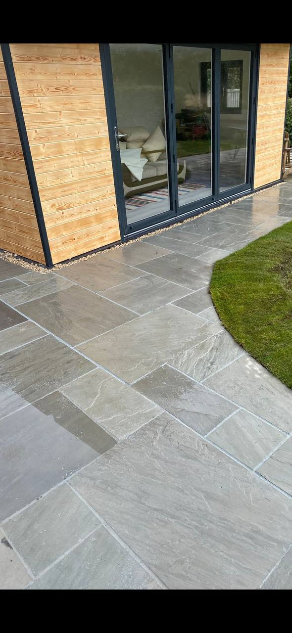 Grey riven slate-effect sandstone patio outside a timber garden room with bifold doors