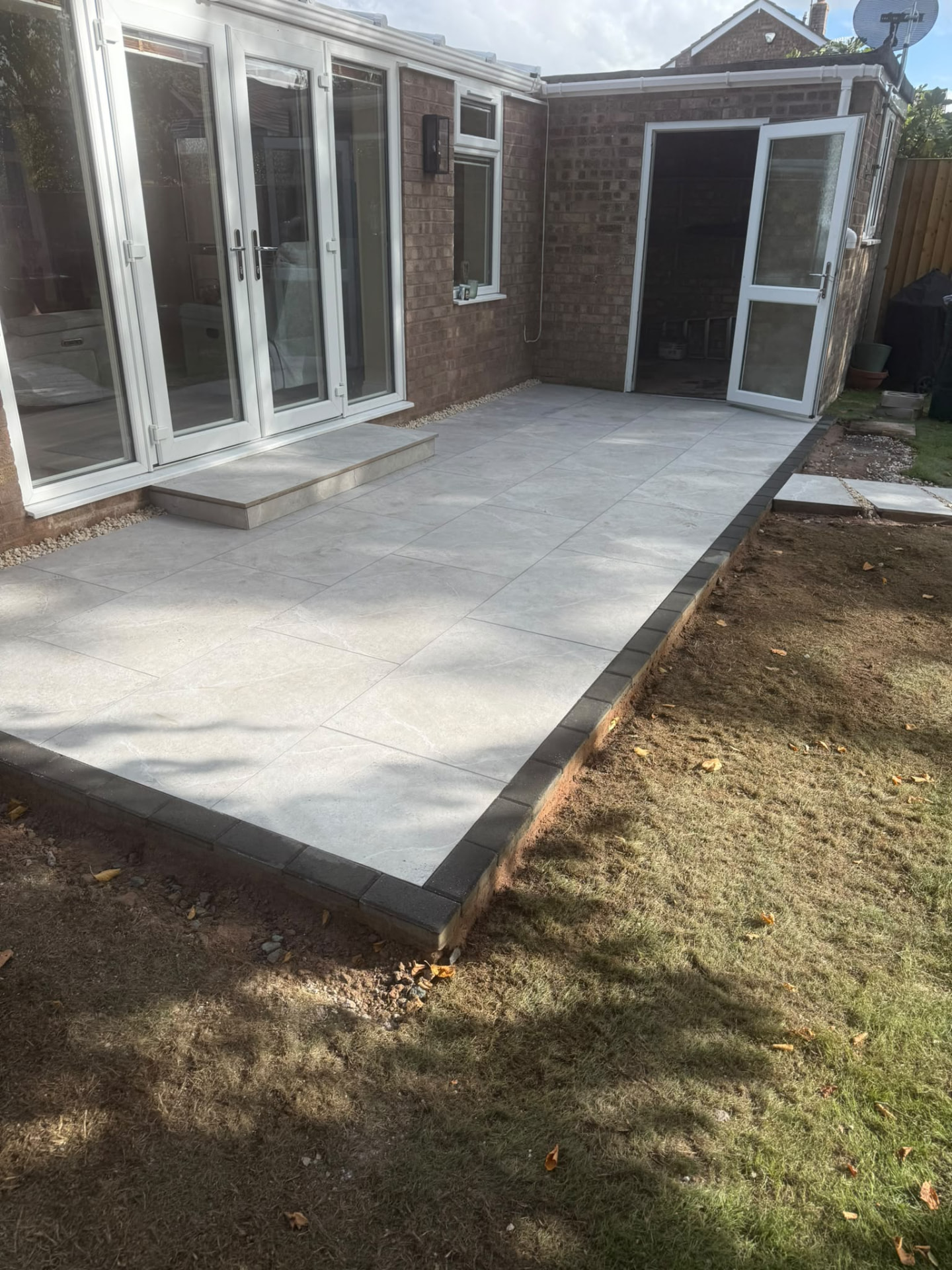 Grey porcelain patio with charcoal block kerb edging and porcelain step outside French doors — Shrewsbury